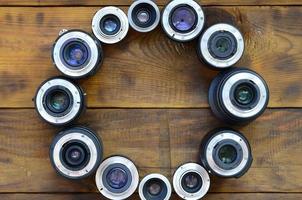 Several photographic lenses lie on a brown wooden background. Space for text photo