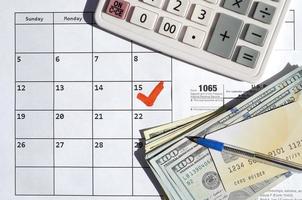 1065 Return of partnership income blank with dollar bills, calculator and pen on calendar page with marked 15th April photo