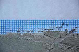 The texture of the wall, covered with gray foam polystyrene plates, covered with a blue reinforcing mesh and covered with a mixture for gluing it. Stage of wall insulation photo