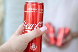 KHARKOV. UKRAINE - MAY 2, 2019 Male hands holds few Coca-Cola tin cans in garage interior and female hand with one can in foreground photo