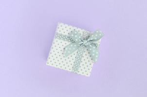 Small white gift box with ribbon lies on a violet background. Minimalism flat lay top view photo