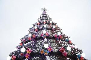 A fragment of a huge Christmas tree with many ornaments, gift boxes and luminous lamps. Photo of a decorated Christmas tree close-up with copy space