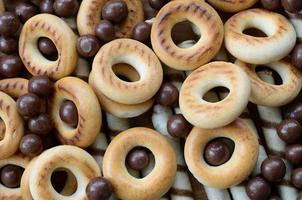 A lot of crispy sweet tubules, chocolate melting balls and yellow bagels lie on a wooden surface. Close up view photo