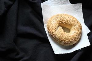 The bagel is placed on white paper and black cloth. photo