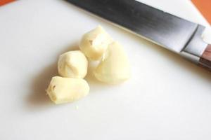 Ginger is being sliced on a plastic chopping board with a knife on an orange table. photo