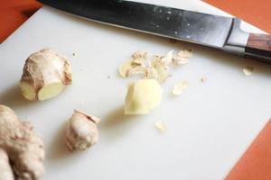 Ginger is being sliced on a plastic chopping board with a knife on an orange table. photo