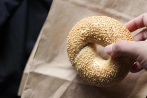 A man's hand is holding a bagel on a brown paper bag. photo