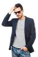 Confident in his style. Handsome young man wearing sunglasses holding hand in hair while standing against white background photo