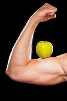 Healthy lifestyle. Cropped image of muscular man showing his perfect biceps with a green apple on it while isolated on grey background photo