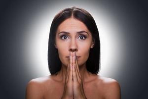 Begging for... Portrait of frustrated young shirtless woman looking at camera and keeping hands clasped near face while standing against grey background photo