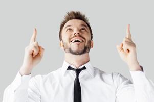 Thanks to God Handsome young man in shirt and tie pointing up and smiling while standing against grey background photo