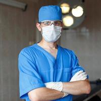 cirujano con uniforme azul, gafas y sombreros en el quirófano al fondo de luces brillantes foto