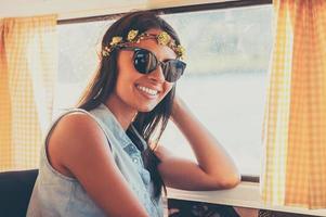 Flower child in the sun. Happy young woman smiling at camera while sitting inside of the retro van photo