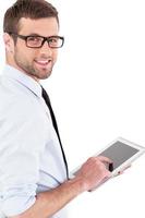 Confident and experienced businessman. Cheerful young man in formalwear working on digital tablet and looking over shoulder while standing isolated on white background photo