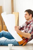 Examining blueprint. Confident young handyman examining blueprint while sitting on the floor photo