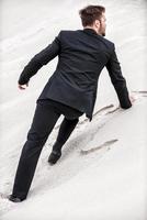 Businessman on desert dune. Rear view of young man in formalwear rising up by desert dune photo