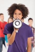 Hey you Young African teenager shouting at megaphone while his friends standing on background photo