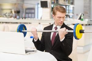 I choose healthy lifestyle. Confident young red hair man in formalwear sitting at the restaurant and holding a dumbbell photo