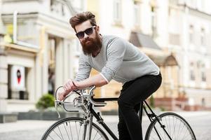 Es hora de salir a la carretera. apuesto joven barbudo mirando a la cámara mientras se sienta en su bicicleta al aire libre foto