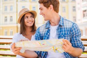 elegir un lugar para ir. feliz pareja de jóvenes turistas sentados juntos en el banco y examinando el mapa foto