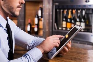 Surfing web in bar. Close-up of man in shirt and tie working on digital tablet while sitting at the bar counter photo