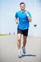 I love running. Full length front view of handsome young man running along the road and smiling photo