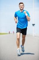 me encanta correr. vista frontal completa de un joven apuesto corriendo por la carretera y sonriendo foto