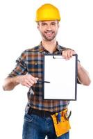 I need your signature here. Cheerful young male carpenter holding clipboard and pointing it with pen while standing against white background photo