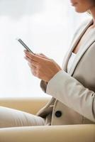 Typing business message. Side view of businesswoman in suit typing something on mobile phone while sitting at the chair photo