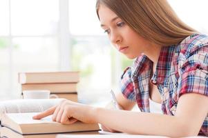 estudiando duro. vista lateral de una adolescente segura de sí misma estudiando mientras se sienta en el escritorio foto