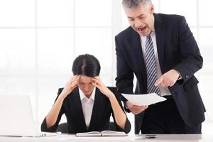 You are doing it all wrong Furious mature businessman holding document and shouting while depressed woman sitting at the table and holding head in hands photo