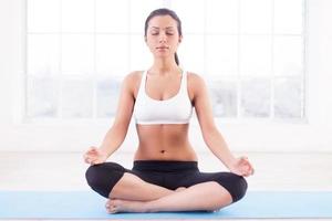 Feeling calm. Beautiful young Indian woman mediating while sitting in lotus position photo