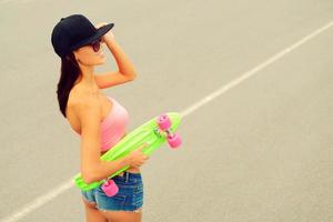 genial chica patinadora. vista superior de una hermosa joven sonriente sosteniendo su colorida patineta y sonriendo foto