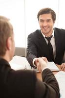 Welcome to team. Two business men shaking hands and smiling while sitting at the table photo