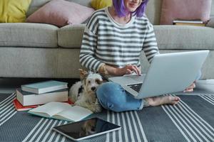 primer plano de una adolescente usando una laptop en casa mientras un lindo perrito sentado cerca de ella foto