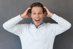 That is unbelievable Surprised mature man touching head with hands and expressing positivity while standing against grey background photo