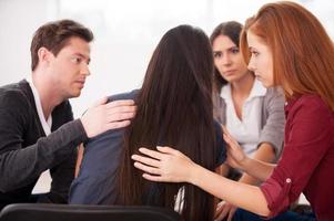 We understand you. Rear view of depressed young woman sitting at the chair while other people comforting her photo