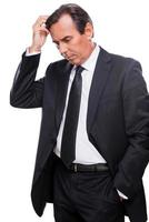 Lost in business thoughts. Worried mature man in formalwear holding hand in hair and looking away while standing isolated on white background photo