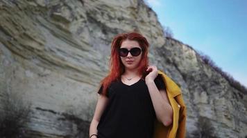Beautiful fashionable woman in sunglasses posing in front of the camera against the backdrop of mountains. Lifestyle and travel. Slow motion. video