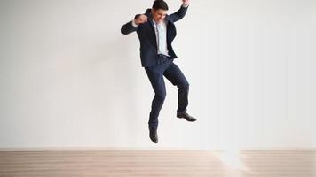 divertido hombre de negocios bailando de alegría y éxito sobre un fondo blanco. trabajador de oficina feliz en ropa formal se ríe y salta con felicidad de victoria. emociones de un ganador, crecimiento profesional. video