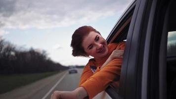 Happy Beautiful Girl Riding in the Back Seat of a Car Looks Out the Open Window and Smiles. Traveling Woman Enjoys the Stunning Scenery. Slow Motion. video