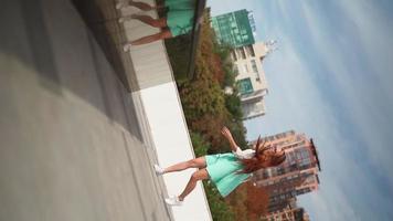 A beautiful slim woman in a trendy turquoise suit is spinning with happiness against the background of the city. Pretty, playful lady rejoices at her success in the downtown area. Slow motion. video