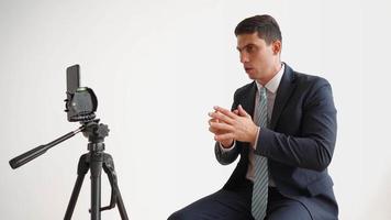 Business man in formal clothes, jacket and tie, is broadcasting live using a mobile phone in the office on a white background. Employee online training concept. video