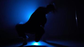 Silhouette, man street dancer dancing stylish dance in a smoky room with backing blue neon light.