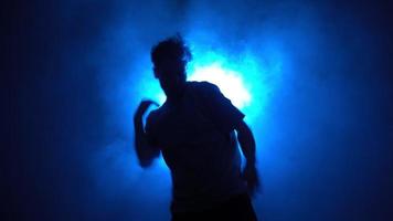 Silhouette, man street dancer dancing stylish dance in a smoky room with backing blue neon light.