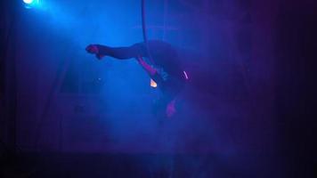 silhuett, kvinna antenn gymnast utför en lura i de ringa i en rökig rum med bakgrundsbelyst blå ljus. neon belysning. video