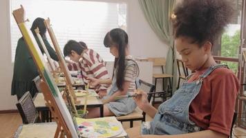 Eine Gruppe gemischtrassiger Kinder, die mit einer Asiatin lernen, lehrt das Malen von Acrylbildern auf Leinwand im Kunstklassenzimmer und lernt kreativ mit Geschick in der Studioausbildung der Grundschule. video