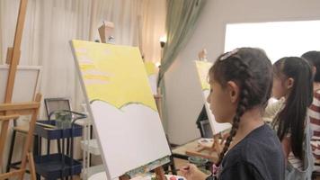 una niña pequeña se concentra en la pintura acrílica en color sobre lienzo con niños multirraciales en un aula de arte, aprendizaje creativo con talentos y habilidades en la educación de estudio de la escuela primaria. video