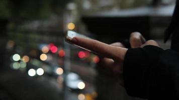 la mano de una joven está enviando mensajes de texto a un teléfono móvil bajo la lluvia y el tráfico borroso video