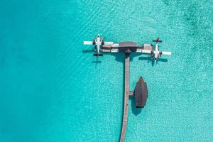 Hydroplane in the crystal clear turquoise water Indian Ocean tropical islands. Top aerial view in Maldives island, water villa and long pier with seaplanes in amazing sea lagoon. Fantastic travel photo